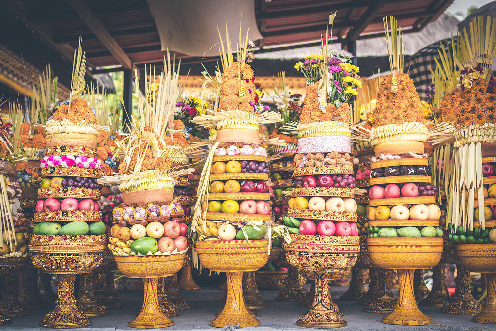 Gebogan — tall, tiered offerings of fruit and cake — lined up for a temple ceremony, the kind women carry to the temple on their heads.