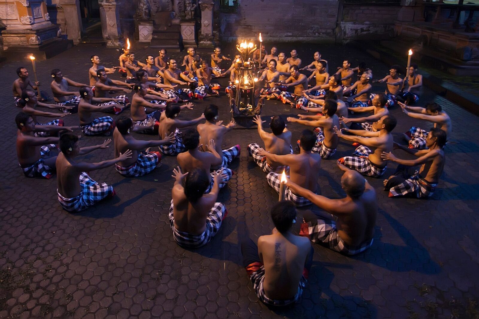 The Kecak from above — a ring of chanting men around a central lamp at dusk.