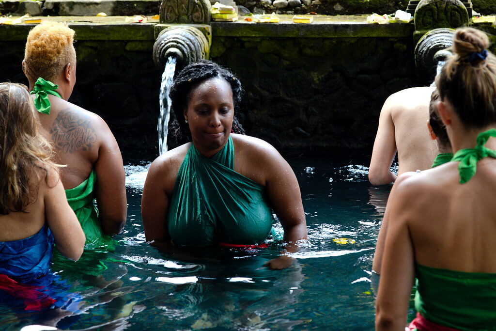 A woman taking her turn under the spouts in a wet sarong; visitors can often join respectfully, with guidance.