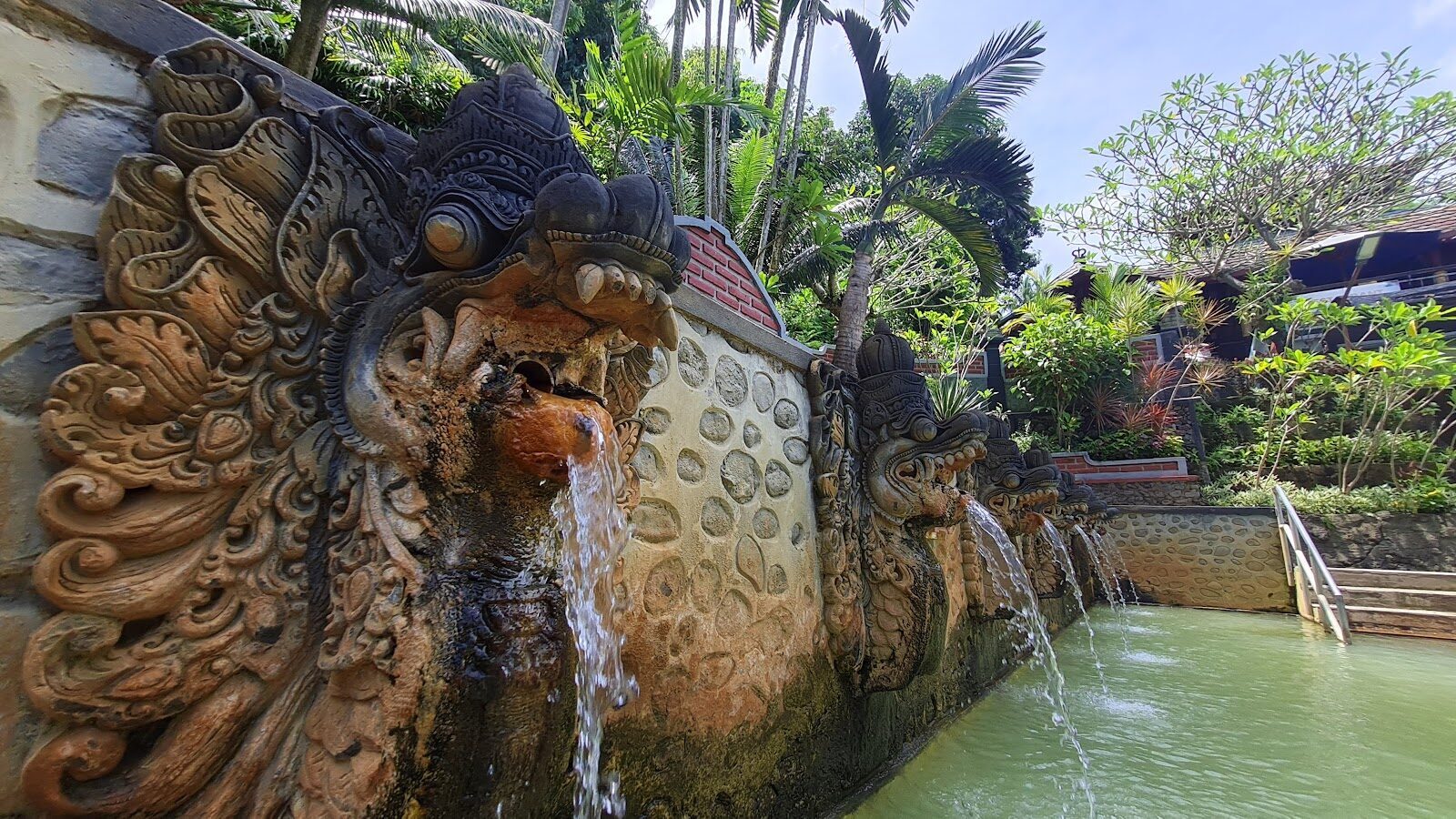 Water pours from a carved stone naga (dragon) mouth — the springs' signature detail.