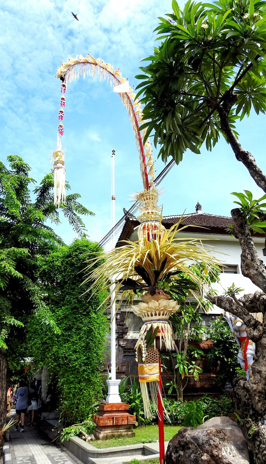 A single tall penjor curving against a blue sky beside the palms.