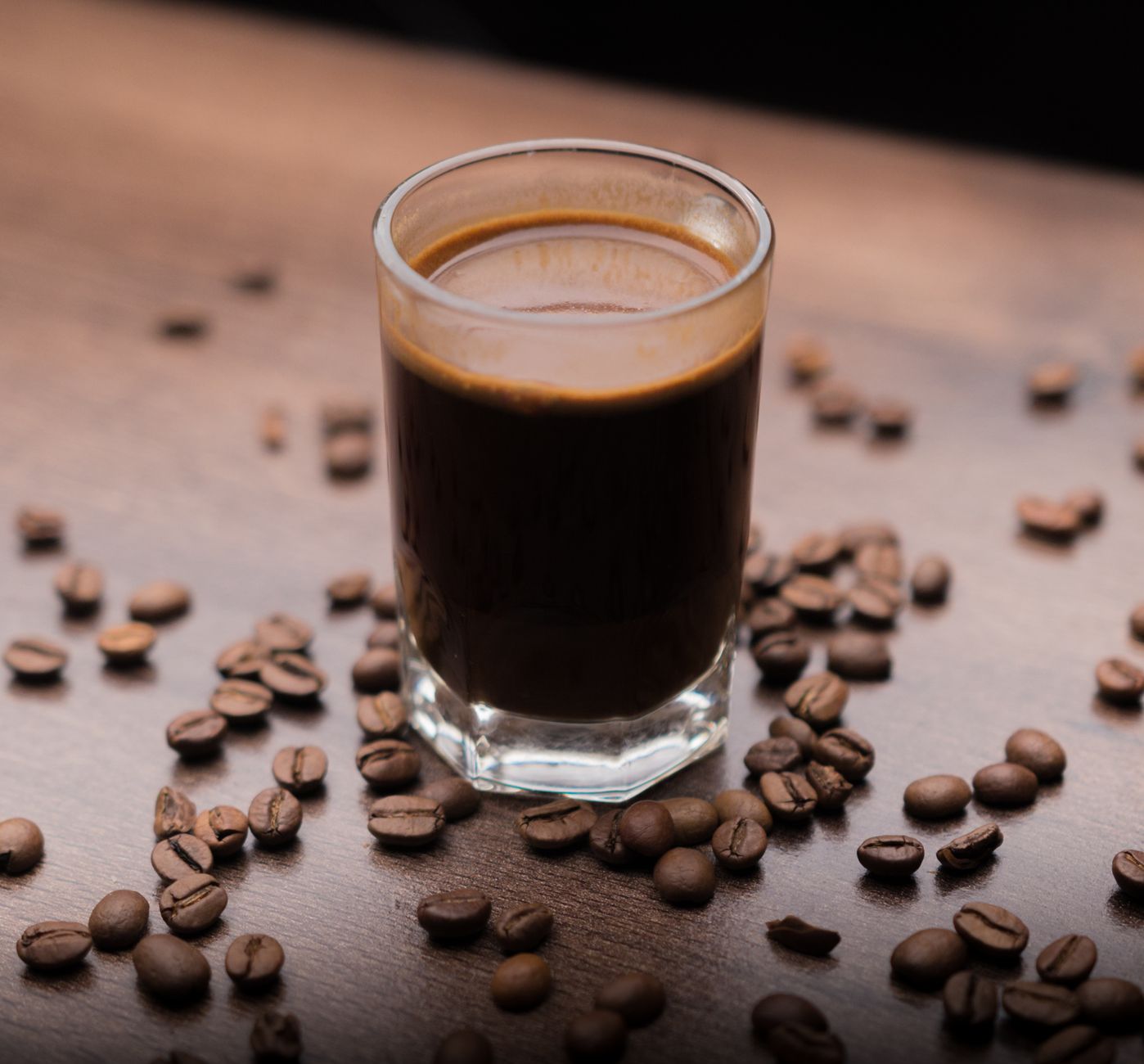 A glass of black coffee surrounded by roasted beans