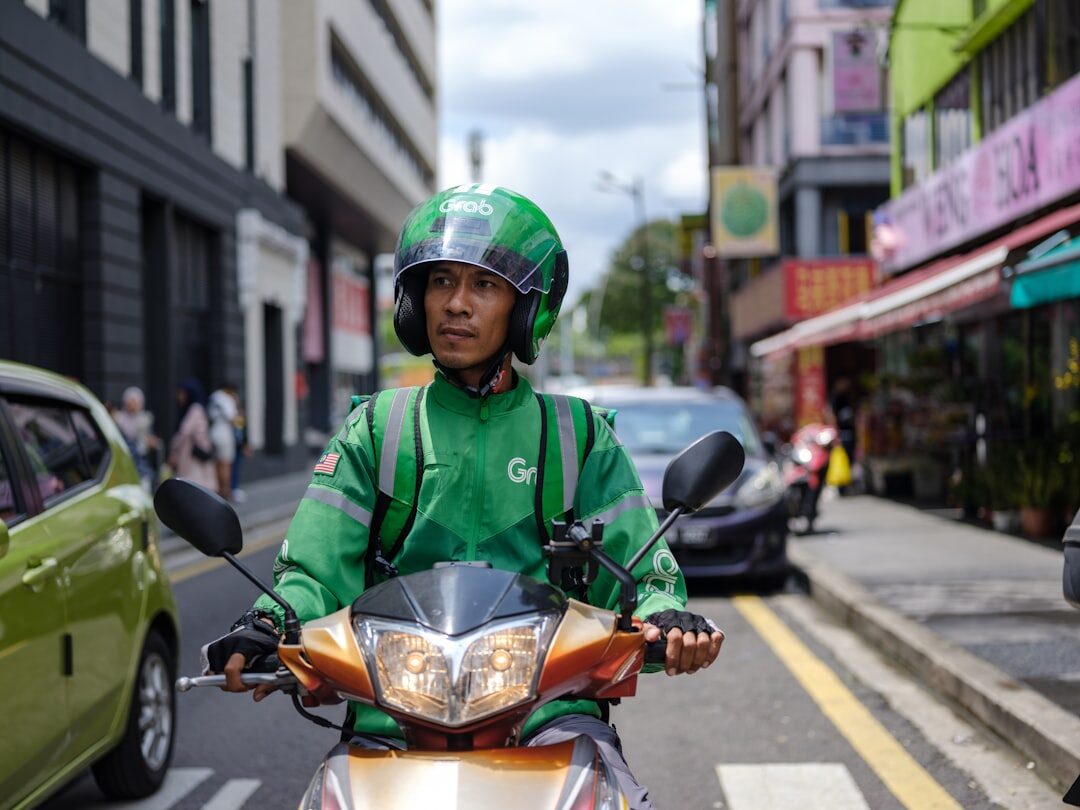 A driver in the green app jacket on his scooter, helmet on, ready for a fare.