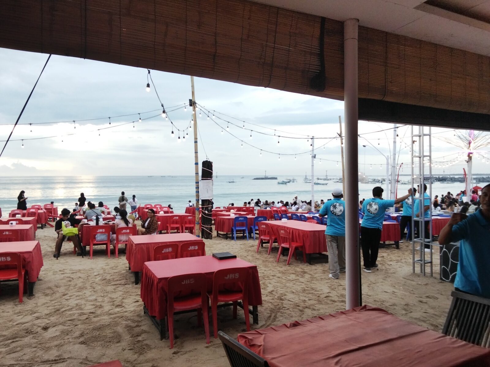 Tables dressed in red cloth set out in the sand at dusk, strung with lights, the classic Jimbaran sunset-dinner setting.