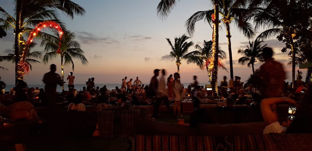 Diners silhouetted under the palms as the sky fades over the bay.