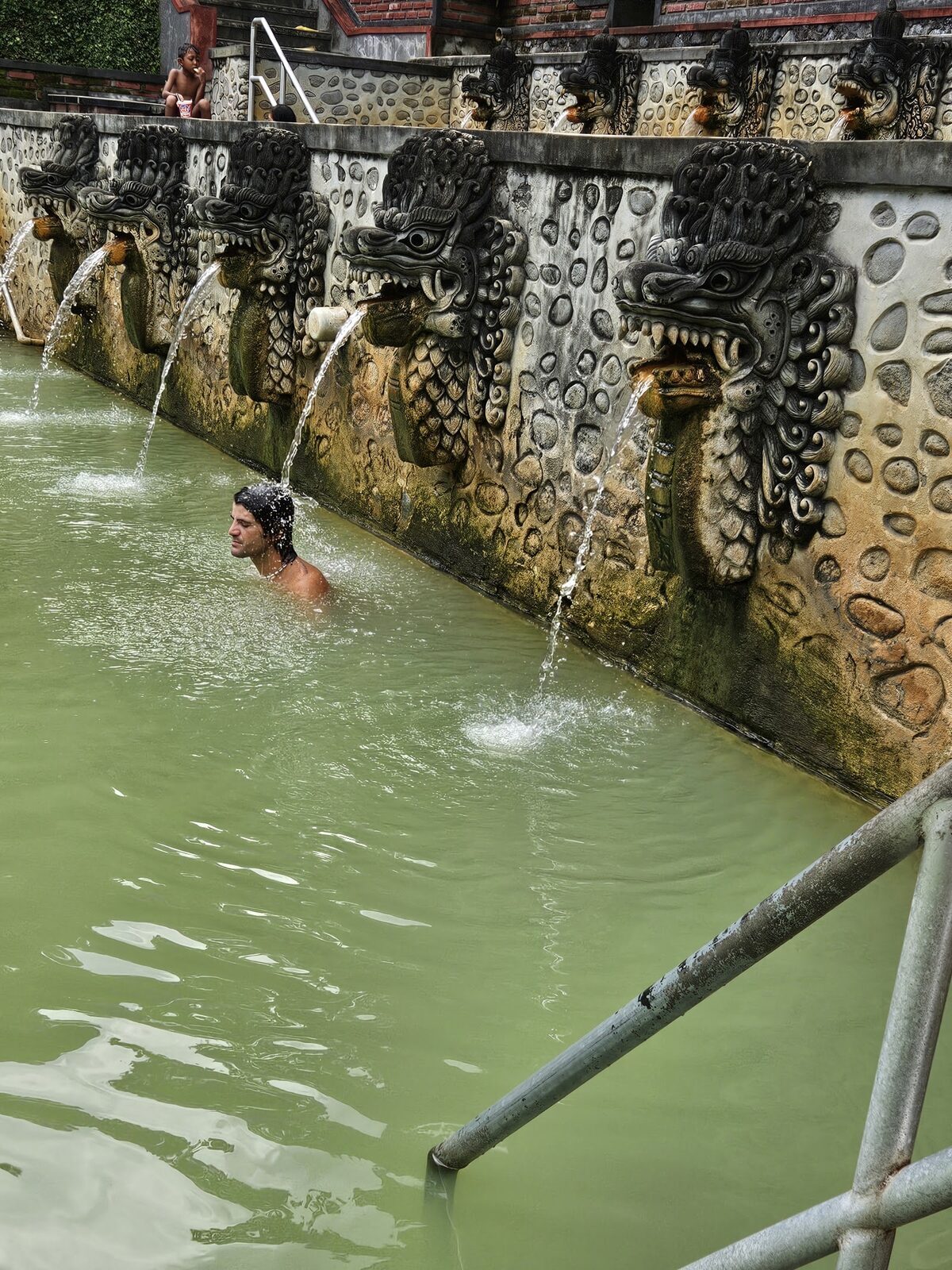 A bather under one of Banjar's dragon-mouth spouts — the warm sulphur water everyone comes to sit beneath.