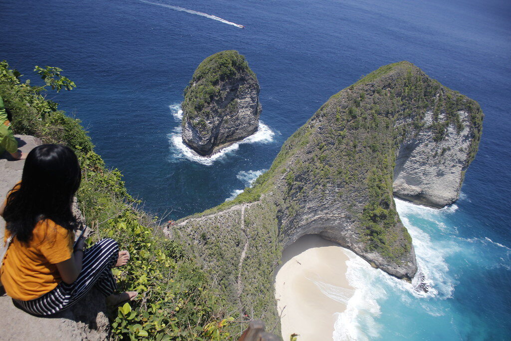 A visitor at the clifftop viewpoint, the T-rex cliff across the bay — the free, five-minute payoff.