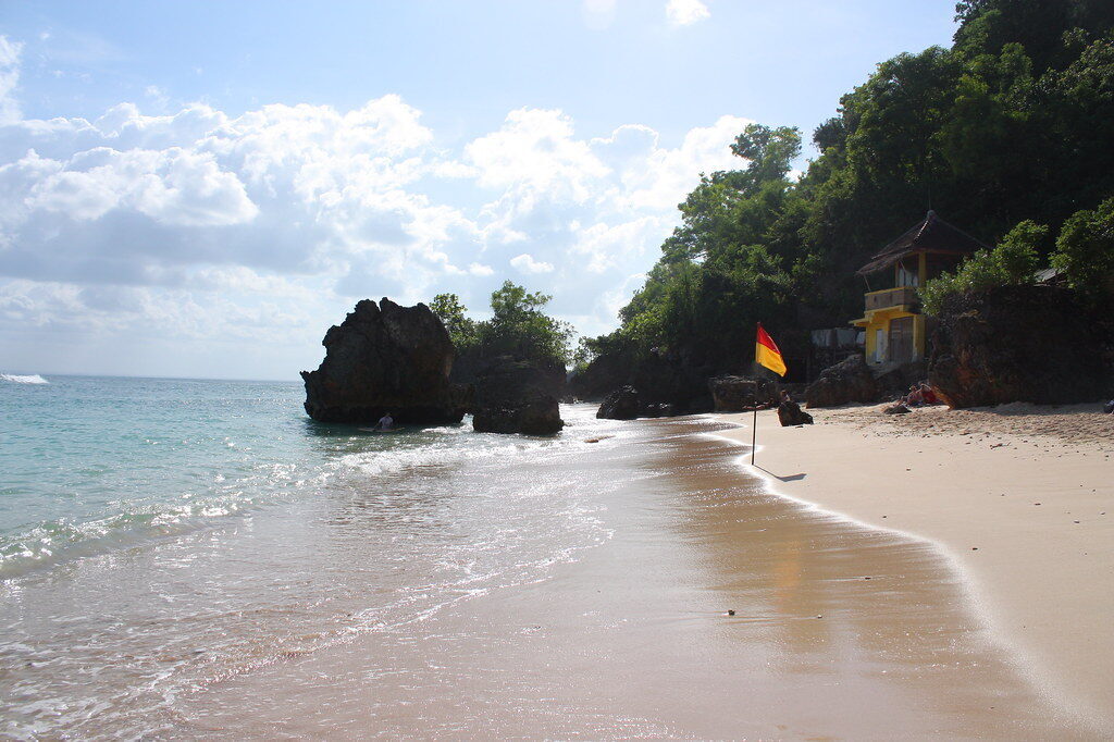 The cove's turquoise water and rock headland, flags marking the warungs.