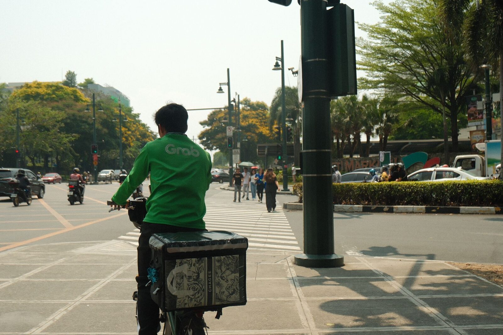 A ride-hailing rider with a delivery box waits at a crossing.