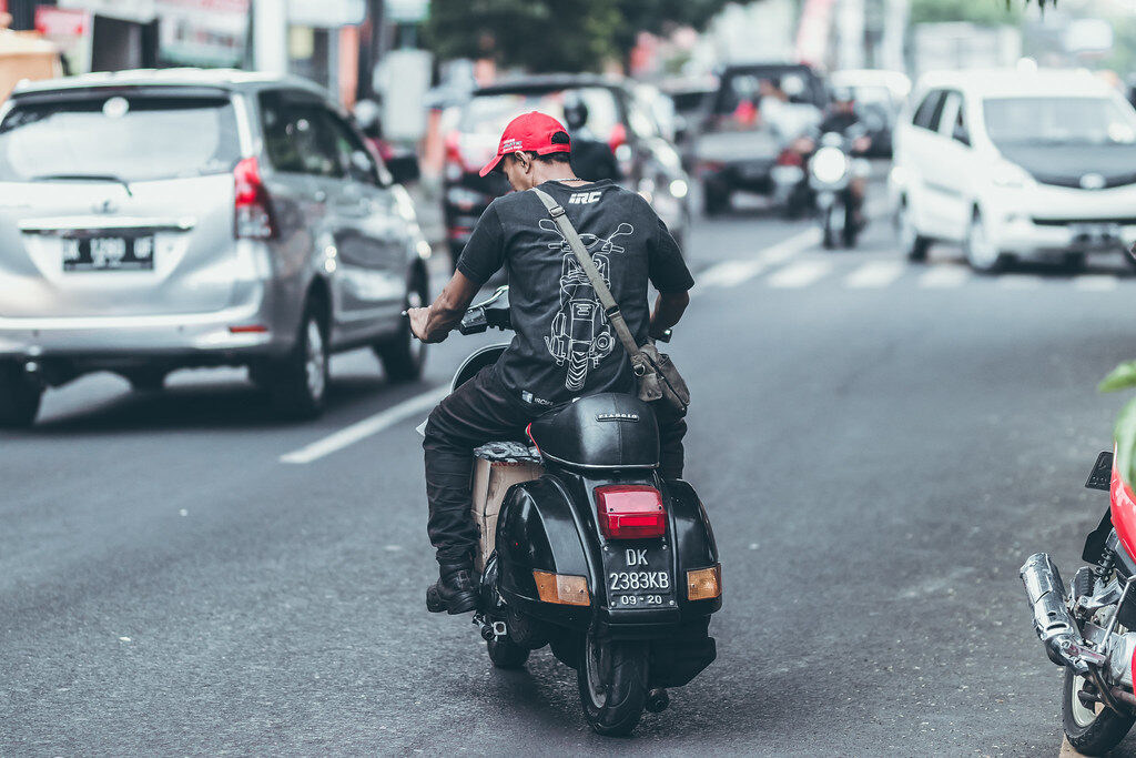 A rider weaves a scooter between cars on a busy street.