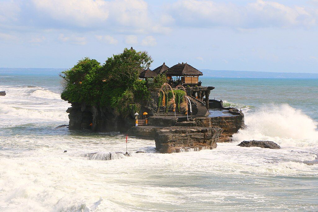 The sea temple mid-tide, visitors small on the rocks below it.