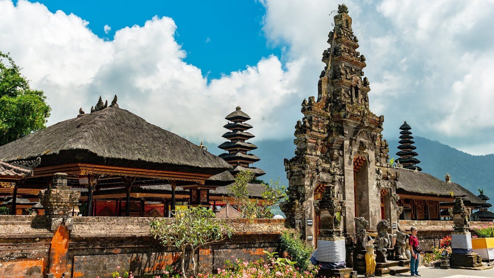 A pavilion and a carved split gate in the temple gardens under a bright sky.