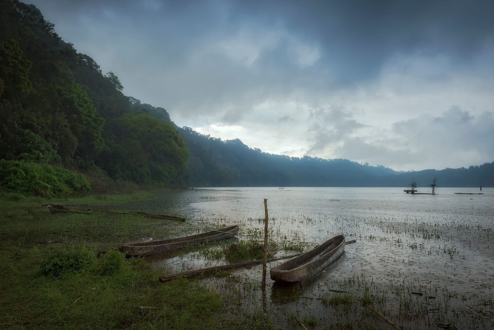 A quiet highland lake in the hills near Bedugul, boats moored under low cloud.