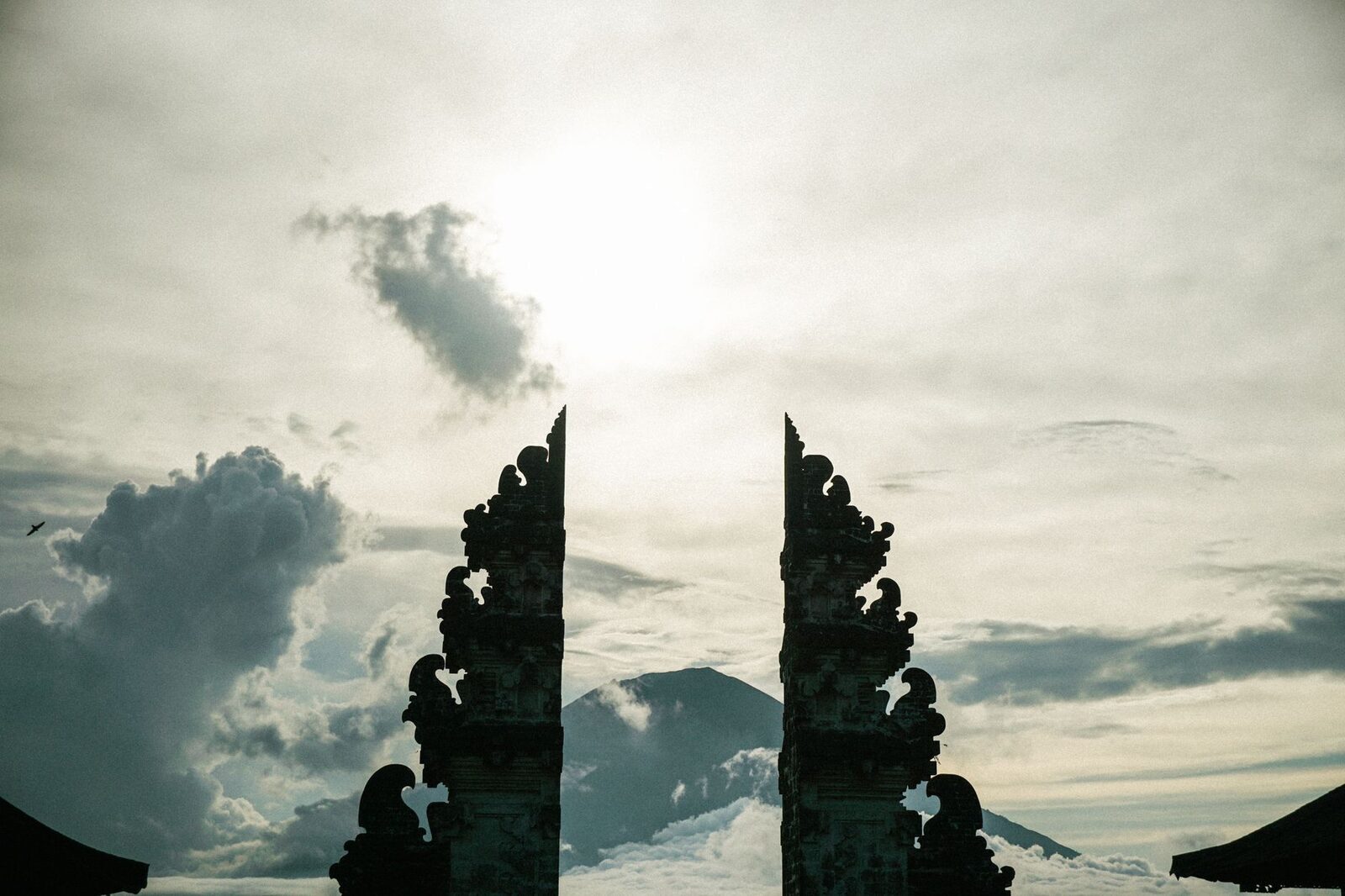 A candi bentar silhouetted against a heavy sky — the drama of the cleaved threshold.