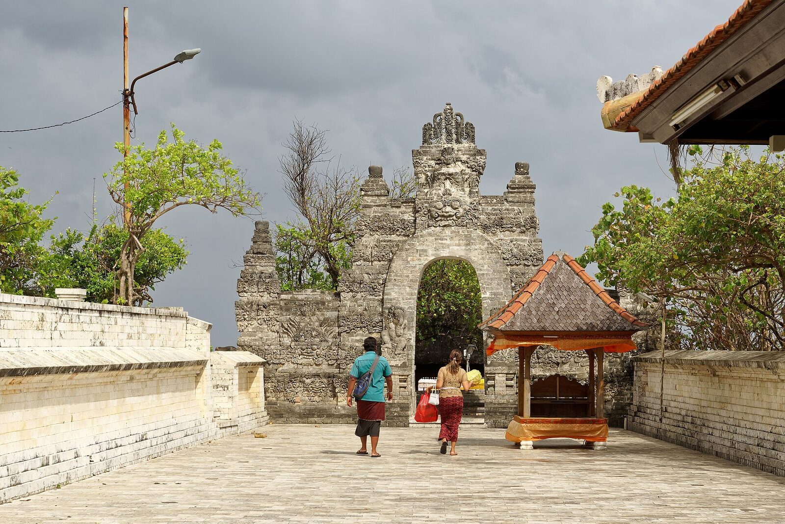 A carved stone gateway at Pura Luhur Uluwatu, worshippers arriving with offerings