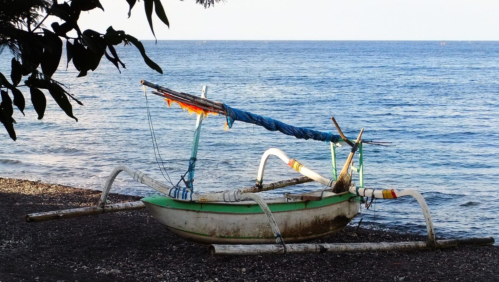 A traditional jukung outrigger drawn up on a dark-sand beach.