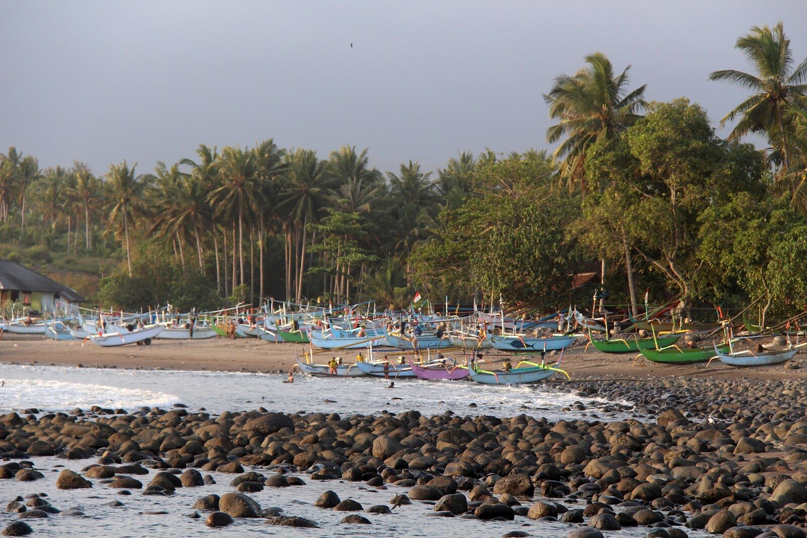 The black-sand, cobble-and-palm point at Medewi, fishing boats pulled up on the beach — far from the Bukit surf crowds.