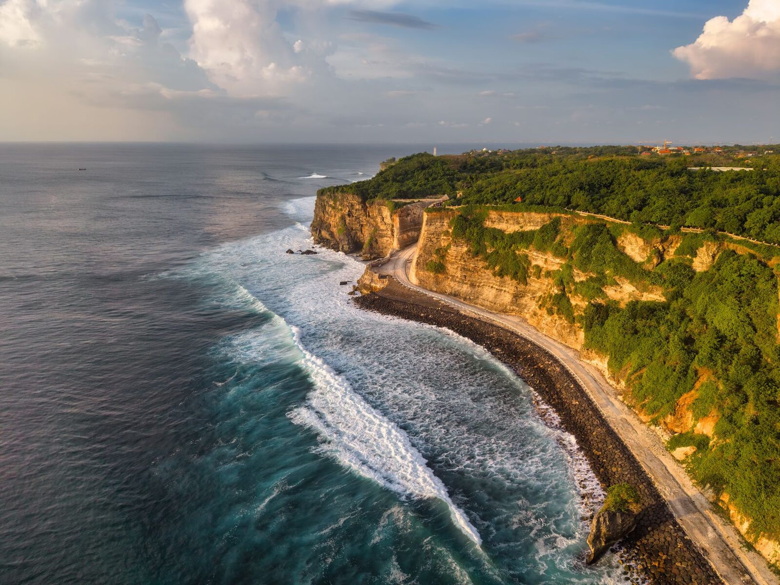 The Bukit's limestone cliffs running gold at the end of the day — the far south's signature, high and sheer above the reef.
