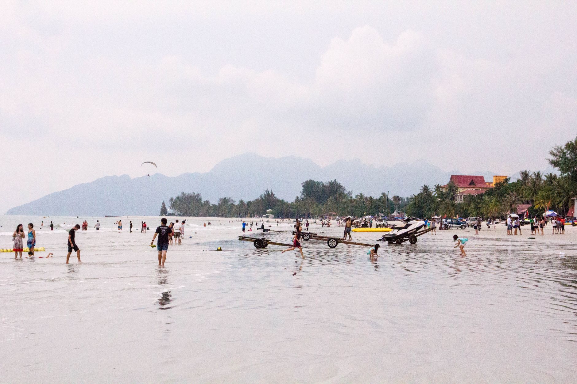A bright beach day with people on the sand at Pantai Cenang.